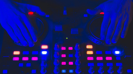 DJ plays music. sound mixer controller with knobs and sliders. hands on the mixing deck with turntables at dark with illuminated controls