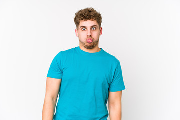 Obraz premium Young blond curly hair caucasian man isolated blows cheeks, has tired expression. Facial expression concept.