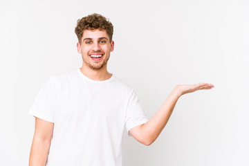 Young blond curly hair caucasian man isolated showing a copy space on a palm and holding another hand on waist.