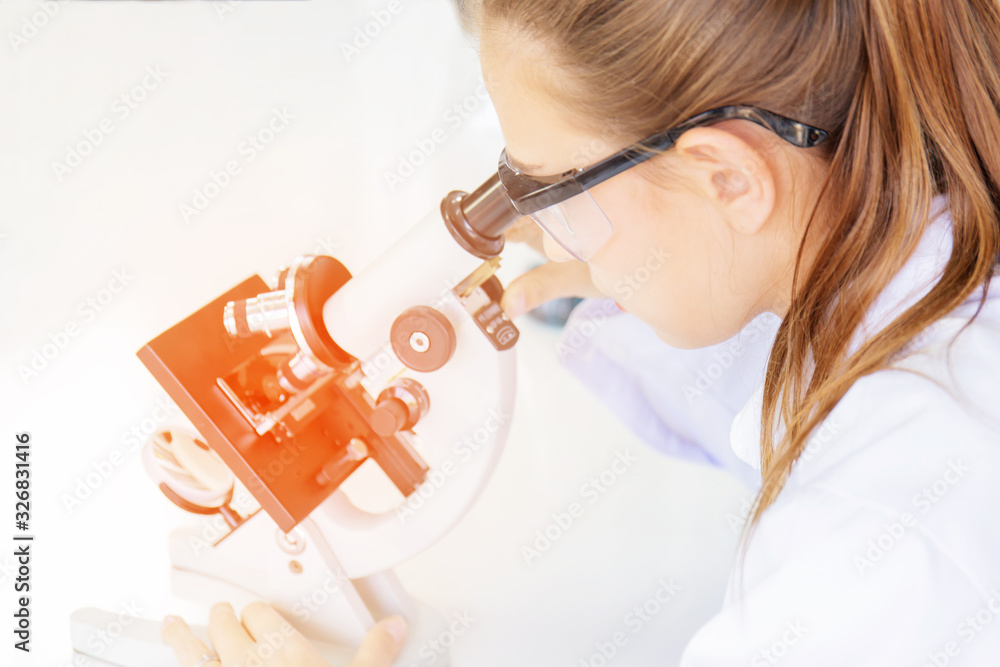 Poster Beautiful female scientists are looking at the microscopes in a science lab with various equipment in the laboratory and have an orange light.