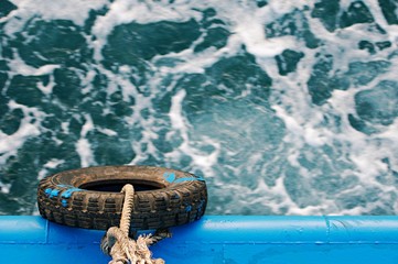 Fototapeta premium Rubber tire using as bumper protect side of boat or ship, bumper hanging on industrial boat for sea, top view and focusing at tire, waving sea water background, transportation concept