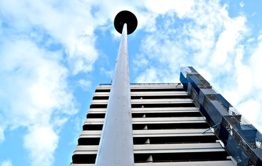 Tall white pole (a lamp post) in front of a modern industrial building. Low angle view of modern architecture with blue sky and white clouds above it.