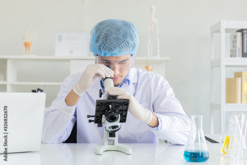 Poster Young Scientist using Microscope in Laboratory. Male Researcher wearing white Coat sitting at Desk and looking at Samples by using Microscope in Lab. Scientist at Work in Laboratory