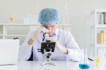 Young Scientist using Microscope in Laboratory. Male Researcher wearing white Coat sitting at Desk and looking at Samples by using Microscope in Lab. Scientist at Work in Laboratory