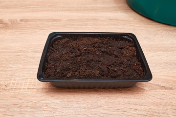 Seeds planted in a plastic box on a wooden table in the house in spring. Seeds in the ground. Seed preparation for planting.