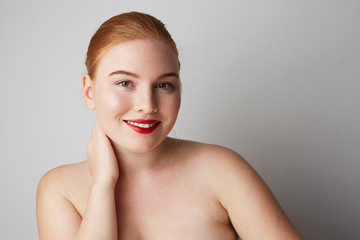 Pretty young woman with naked shoulders and red lips looking at the camera and smiling, posing on the gray wall. Isolated.