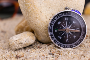 Round compass and a large stone, sand in the background.