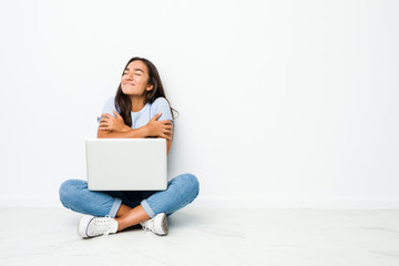 Young mixed race indian woman sitting working on laptop hugs, smiling carefree and happy.