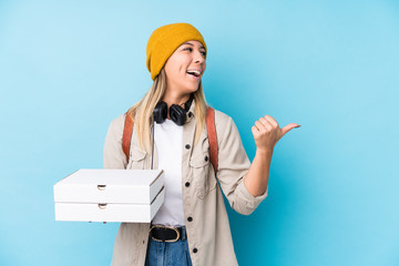 Young caucasian woman holding pizzas isolated points with thumb finger away, laughing and carefree.
