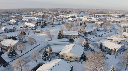 Aerial view of residential houses covered snow at winter season. Establishing shot of american neighborhood, suburb.  Real estate, drone shots, sunny morning, sunlight, from above.