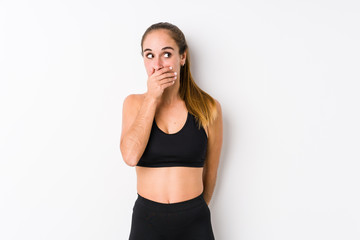 Fototapeta na wymiar Young caucasian fitness woman posing in a white background thoughtful looking to a copy space covering mouth with hand.