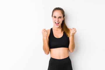 Young caucasian fitness woman posing in a white background cheering carefree and excited. Victory concept.