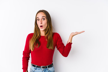 Young caucasian woman posing isolated  impressed holding copy space on palm.