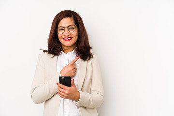 Fototapeta premium Middle age latin woman holding a mobile phone isolated smiling and pointing aside, showing something at blank space.