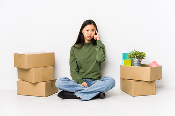 Young chinese woman moving to a new home pointing temple with finger, thinking, focused on a task.