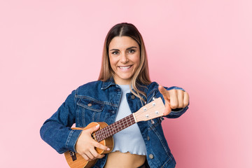 Young caucasian woman playing ukelele cheerful smiles pointing to front.