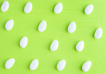 White oval glazed almond candies for bonbonnieres repeating pattern bright photo on light green background. Top view