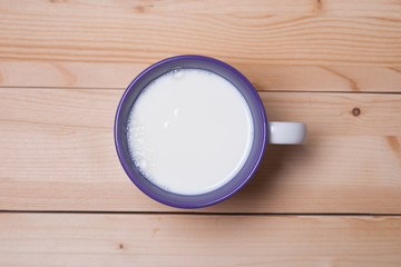 Mug with milk on a wooden surface. View from above. White milk in a purple mug