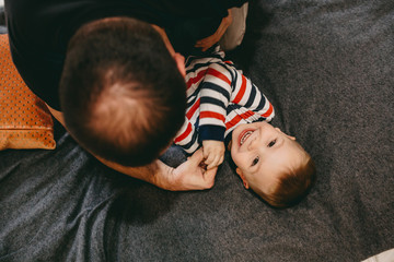 Upper view portrait of a balding caucasian father who is playing on the sofa with his small smiling son