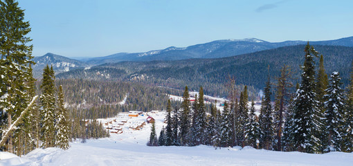 View from the top of the mountain to the ski resort. Siberian winter taiga. Mountain valley