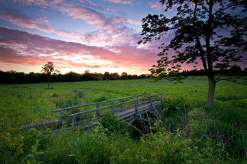 Fototapeta na wymiar A summer sunset sky over a prairie and wooden foot bridge.