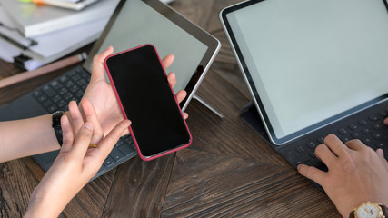 Close up view of businessman typing on mock-up tablet while looking on smartphone