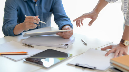 Close up view of two businesspeople briefing on their work on white wooden table in glass wall working space