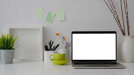 Close up view of workplace with blank screen laptop, stationery, green cup and decorations on white table