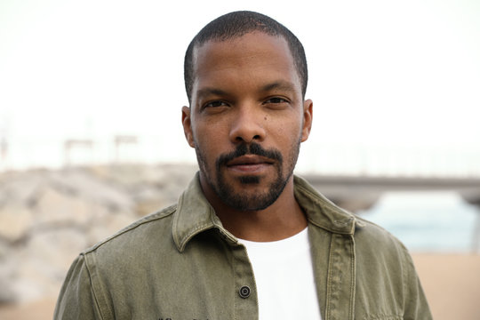 Outdoor portrait of black man looking straight at the camera and wearing casual clothing.