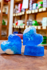 Three blue pieces of handmade soap with white streaks stand on a wooden table against a background...