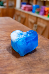 A blue piece of hand-made soap with white streaks lies on a wooden table against a background of...