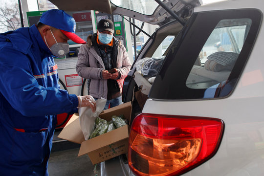 A pump attendant puts a box of groceriees into a car at a Sinopec gas station in Beijing where customers can buy supplies while they refuel