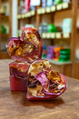 Four pink pieces of handmade soap in the shape of a heart with rose petals lie on a wooden table against a background of wooden counters.