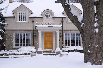 snow covered stucco and stone house with large tree in front yard