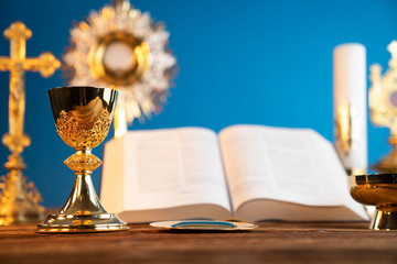 Catholic religion concept. Catholic symbols composition. The Cross, monstrance,  Holy Bible and golden chalice on the altar. Blue background.