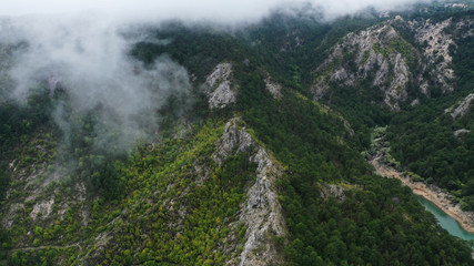 Aerial view of mountains around Lake Grahovo. Clouds on mountain tops. Beautiful landscape of Montenegro nature. Emerald water of Grahovsko Jezero. Forest with green trees. Niksic, Montenegro.
