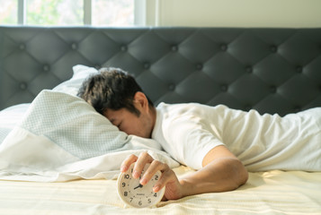 Asian man  wake up in the morning and hand reaching alarm clock