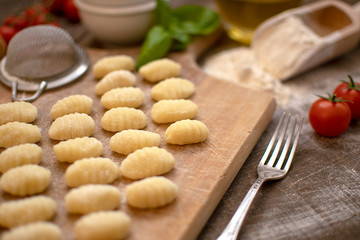 Uncooked homemade potato gnocchi on vintage cutting board over wooden table with flour, selective focus
