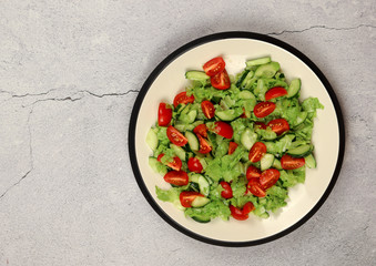 Salad with cherry tomatoes, cucumbers on a plate on a light background. Top view, flat lay