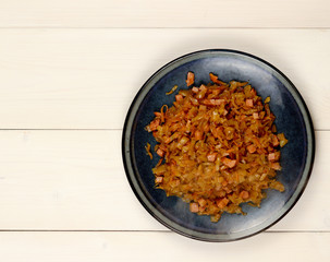 Stewed sauerkraut with sausages on a plate on a light wooden background. Top view, flat lay