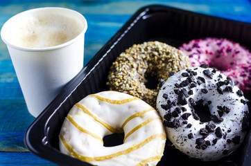 bright colored doughnuts on a dark lining and a paper Cup of coffee on a blue wooden background top view