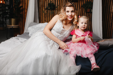 Mother and daughter in the evening dresses sitting on the luxury bed