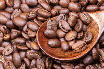 Grains of roasted coffee in a spoon on the table.