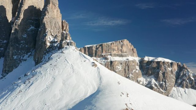 Majestic mountains of Sella massif in Northern Italy. Gray, spiky, snow-covered rocks reaching for the sky. The sky is blue and clear.