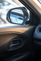 Folded wing mirror of a compact modern car, with a side window glass drop down for ventilation, seeing an inner car door handle. Car parked in a parking lot during the morning time with sun rise.