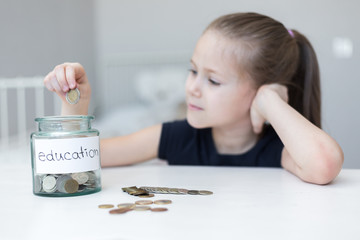 A little girl saves money for education. child counts and puts coins in a glass bottle in her room....