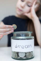 A little girl is saving money for a dream. the child puts coins in a glass bottle. The child saves money on the concept of the future. Selective focus