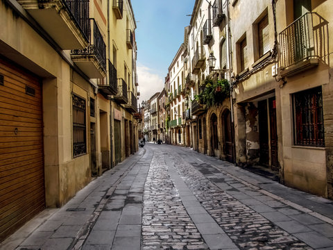 Main street of Carrer Major in the tourist center of the medieval town of Cervera (Catalonia, Spain). Ancient stone residential buildings with balconies on a narrow street, paved with paving stones