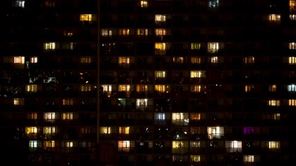 Night time lapse of light in the windows of a multistory building. The light is turned on and off. Countless people live in massive building