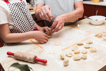 Little girl with grandmother in the kitchen sculpts dumplings